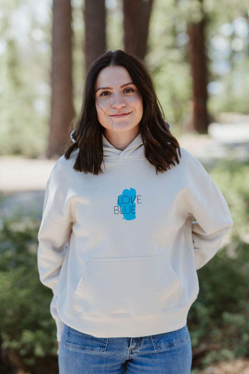 Woman wearing a beige hoodie with a blue logo outdoors
